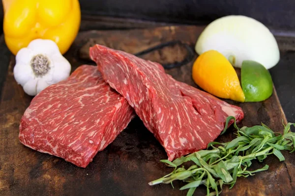 Picture of beef surrounded by vegetables, fruit and herbs on a cutting board