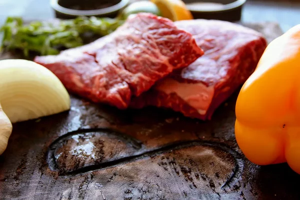 Picture of beef surrounded by vegetables and herbs on a cutting board