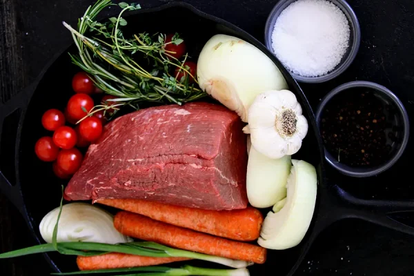 eye of round roast surrounded by veggies in a cast iron pan