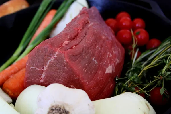 eye of round roast surrounded by veggies in a cast iron pan