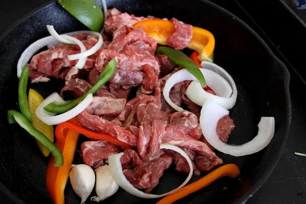 raw beef surrounded by fajita veggies in a cast iron pan