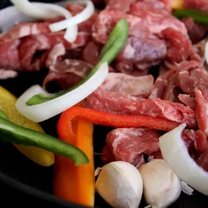 raw beef surrounded by fajita veggies in a cast iron pan