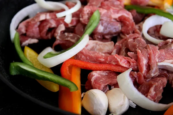 raw beef surrounded by fajita veggies in a cast iron pan