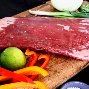 Picture of beef surrounded by vegetables and herbs on a cutting board