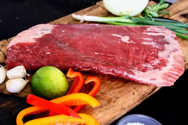 Picture of beef surrounded by vegetables and herbs on a cutting board