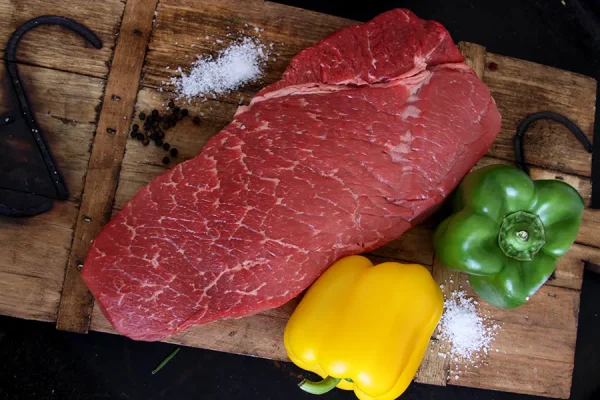 Top london roast surrounded with bell peppers and salt on a Park Ranch branded JP cutting board