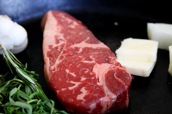 Close up picture of beef surrounded by herbs in a frying pan