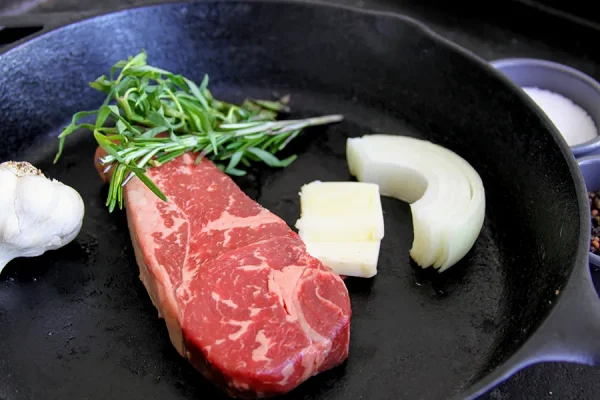 Picture of beef surrounded by herbs in a frying pan