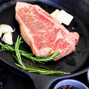 Picture of beef in a frying pan surrounded by herbs