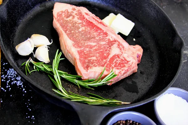 Picture of beef in a frying pan surrounded by herbs