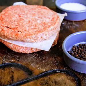 ground beef patties with peppercorns and salt on a Park Ranch branded JP cutting board