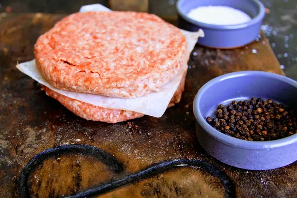 ground beef patties with peppercorns and salt on a Park Ranch branded JP cutting board