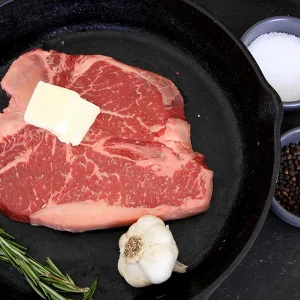 Picture of beef in a frying pan surrounded by herbs and spices