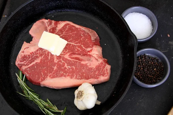 Picture of beef in a frying pan surrounded by herbs and spices