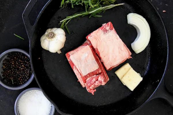 raw short ribs with garlic and other fixings on a cast iron skillet