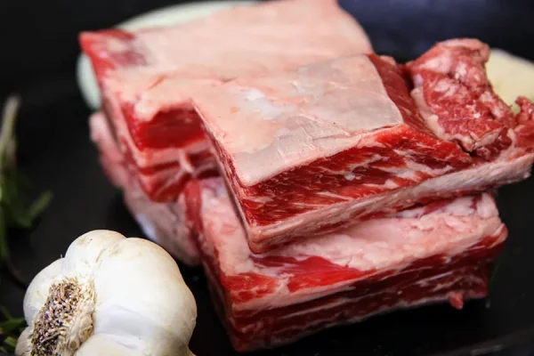 raw short ribs with garlic and other fixings on a cast iron skillet