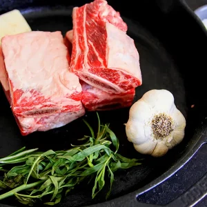 raw short ribs with garlic and other fixings on a cast iron skillet