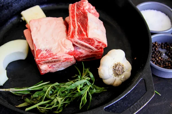 raw short ribs with garlic and other fixings on a cast iron skillet