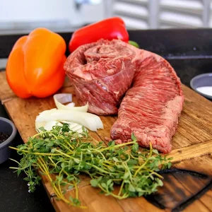 Picture of skirt steak surrounded by vegetables, herbs and spices on a cutting board