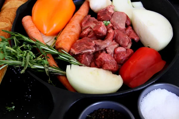 raw stew meat surrounded by veggies in a cast iron pan