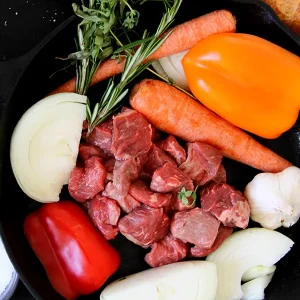 raw stew meat surrounded by veggies in a cast iron pan