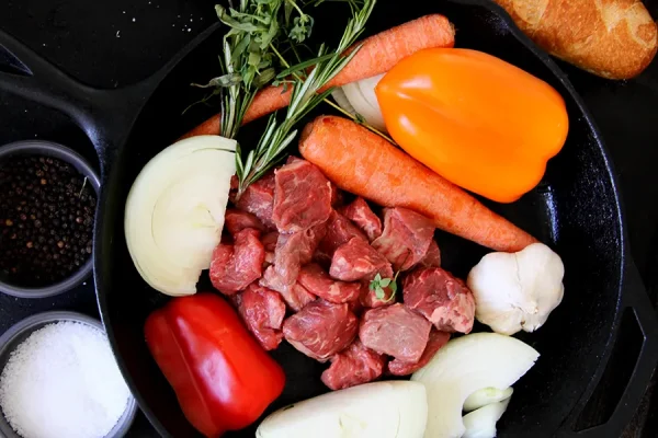 raw stew meat surrounded by veggies in a cast iron pan