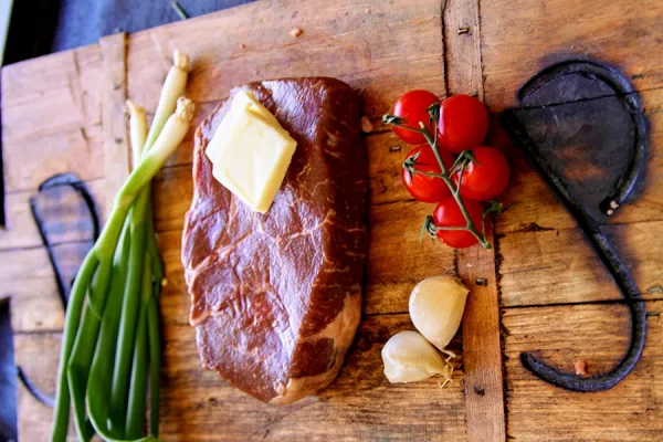 Picture of beef surrounded by vegetables and herbs on a cutting board