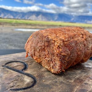 ready-to-cook seasoned boneless prime rib for the holidays displayed outside on a rustic wooden butcher block with JP brand burnt into it - backderop = Colorado Rockies!