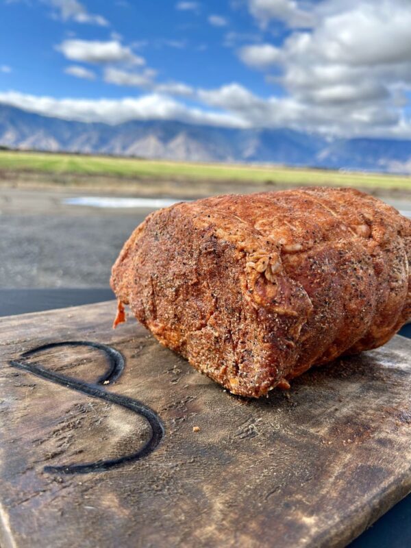 ready-to-cook seasoned boneless prime rib for the holidays displayed outside on a rustic wooden butcher block with JP brand burnt into it - backderop = Colorado Rockies!