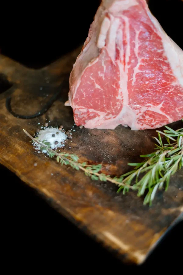 Raw Porterhouse Steak next to salt, pepper, and fresh seasnings